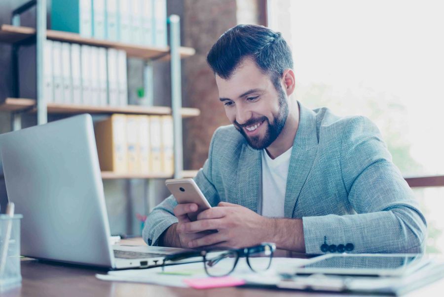 Mann lächelt im Büro auf sein Smartphone